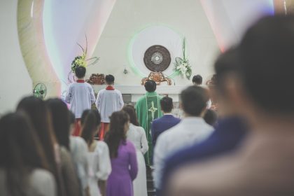 Fiéis participam de uma missa católica em uma igreja, acompanhados por um sacerdote diante do altar.