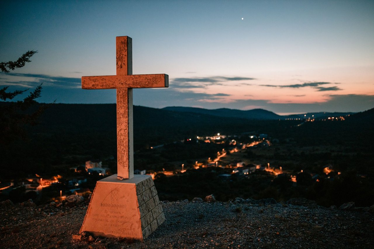 Cruz no alto de uma colina diante de uma aldeia ao entardecer.